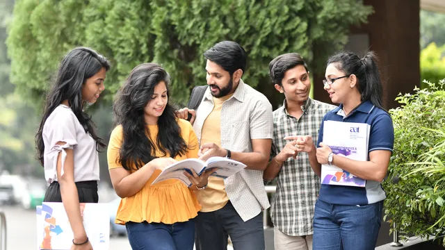Group of university students standing outdoors, reading a book together and discussing academic topics.